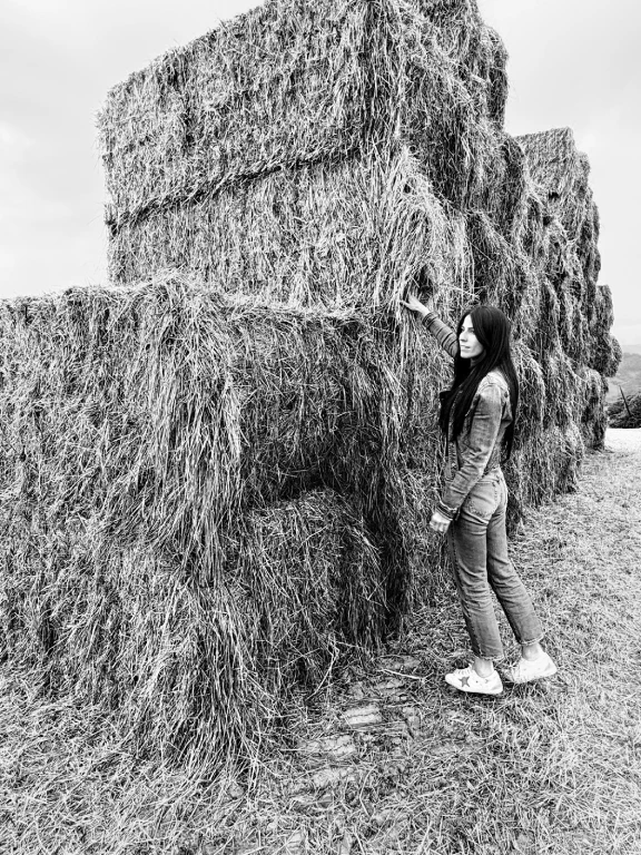 Carlotta Gruppioni in piedi accanto a grandi balle di fieno in campagna, fotografia in bianco e nero.
